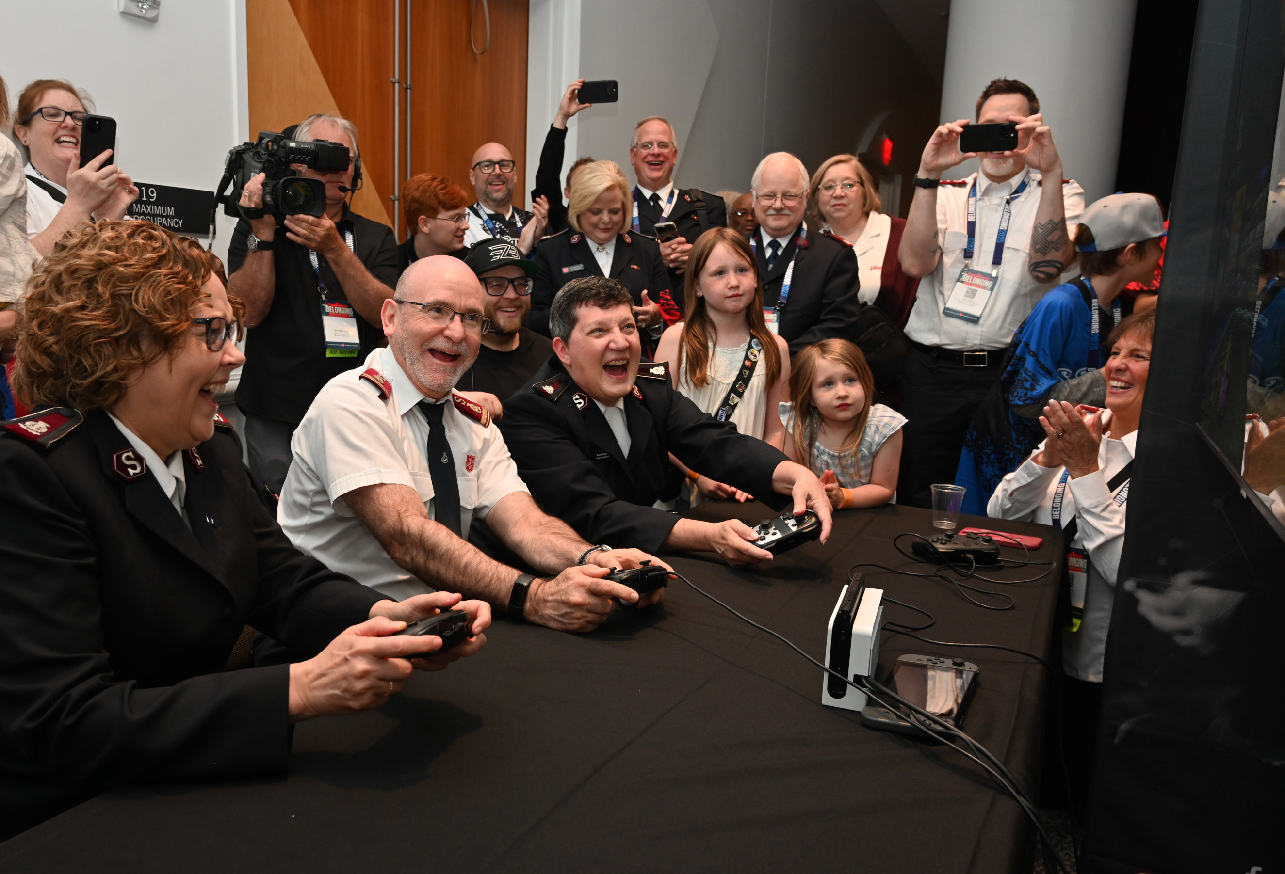 The international leaders laugh as they play a video game surrounded by a crowd
