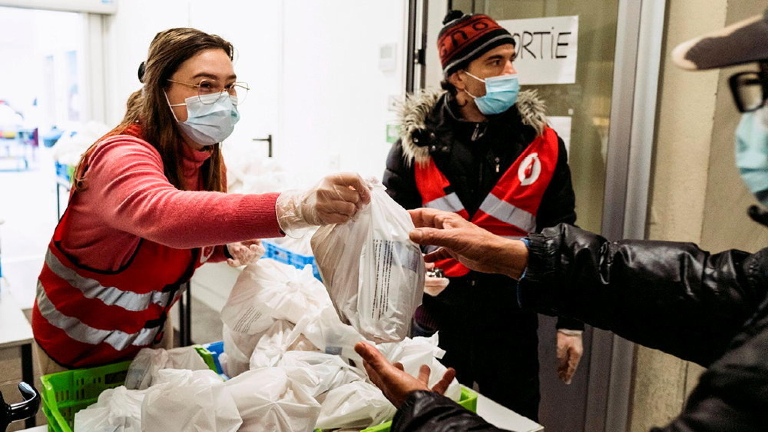 A volunteer hands a carrier bag of goods to a recipient