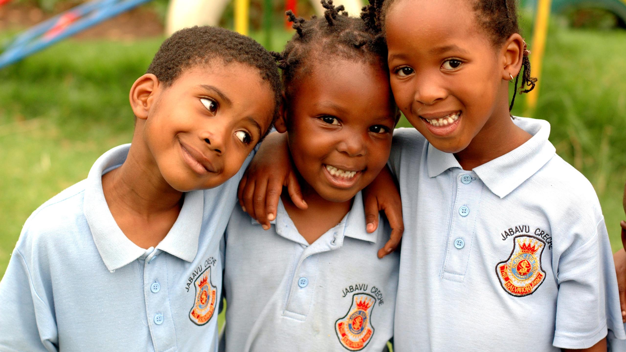 Three young children wearing Salvation Army polo shirts stand with their arms around each other