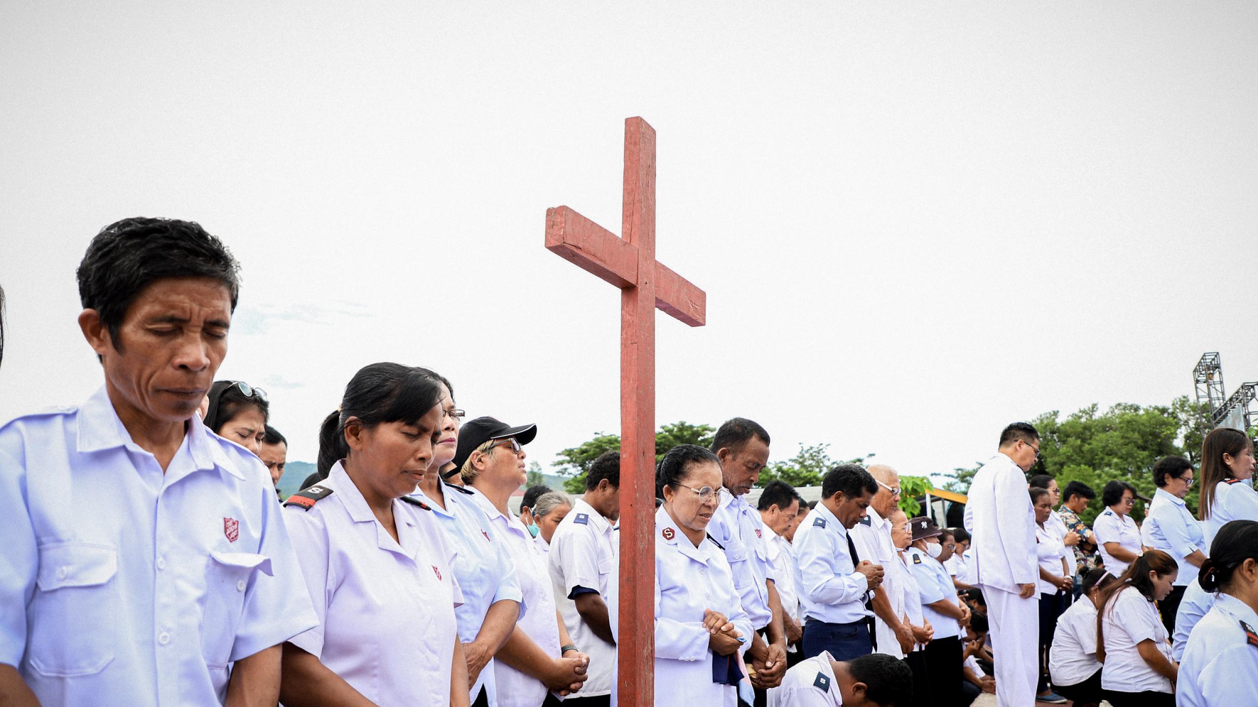 A group of Indonesian Salvationists bow their heads in prayer, gathered around a cross