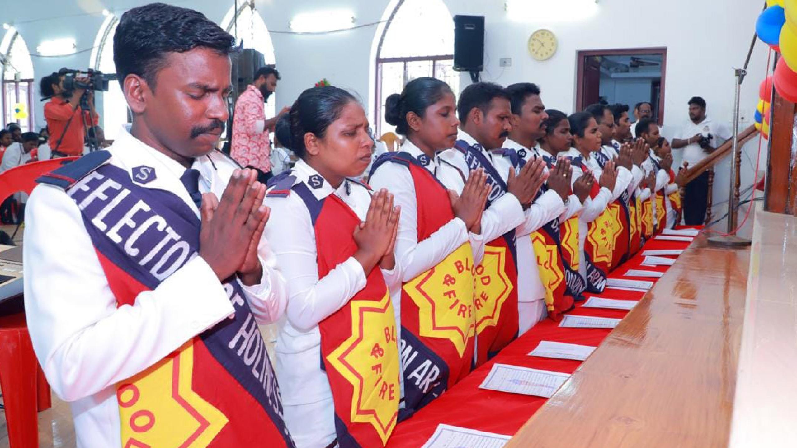Men and women in Salvation Army uniform kneel in prayer