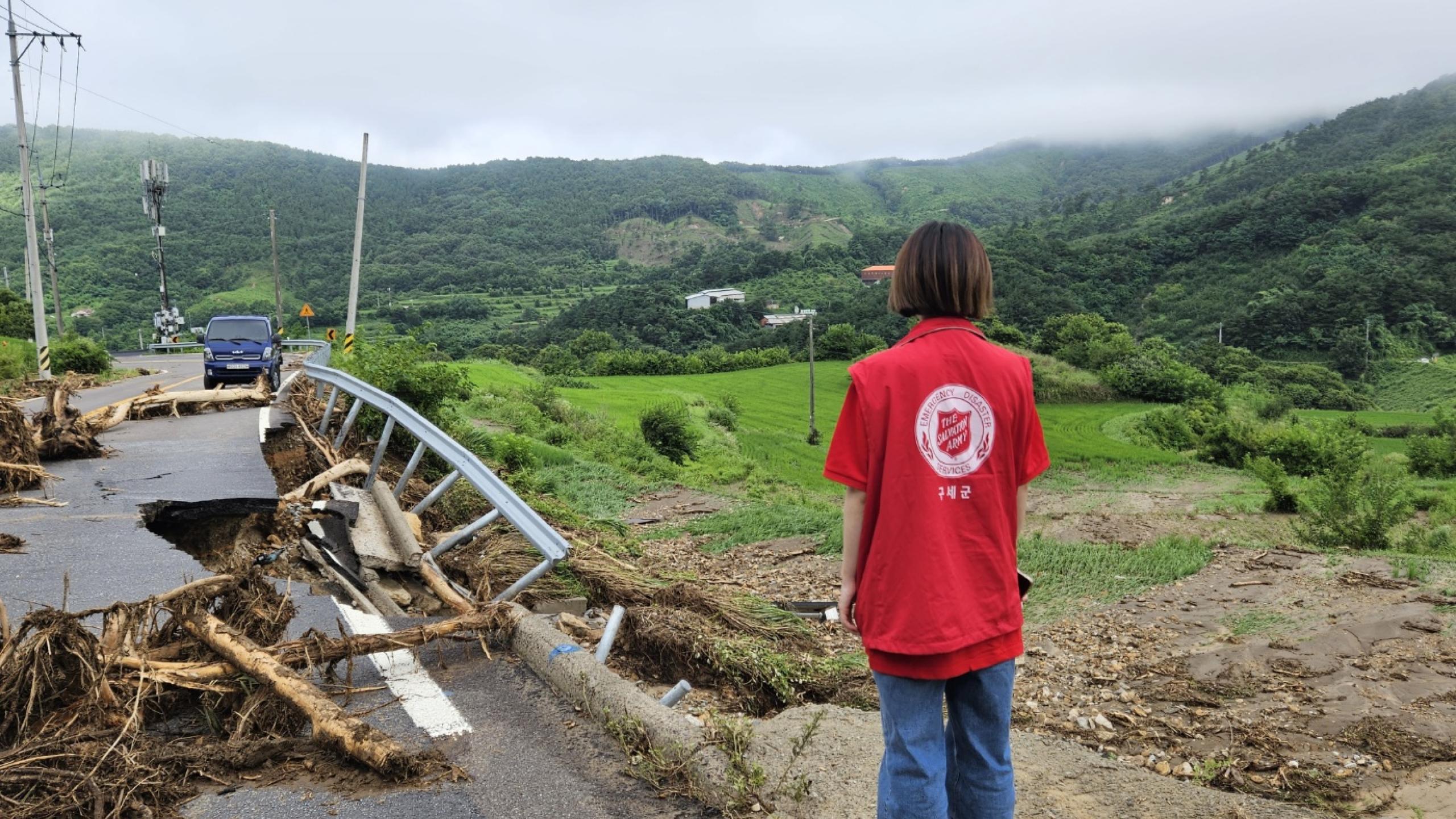 A person in a Salvation Army t-shirt looks out at a flood-damaged road