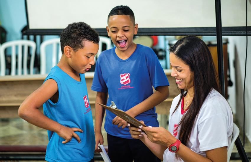 Children in Salvation Army t-shirts laugh together as a volunteer checks a clipboard