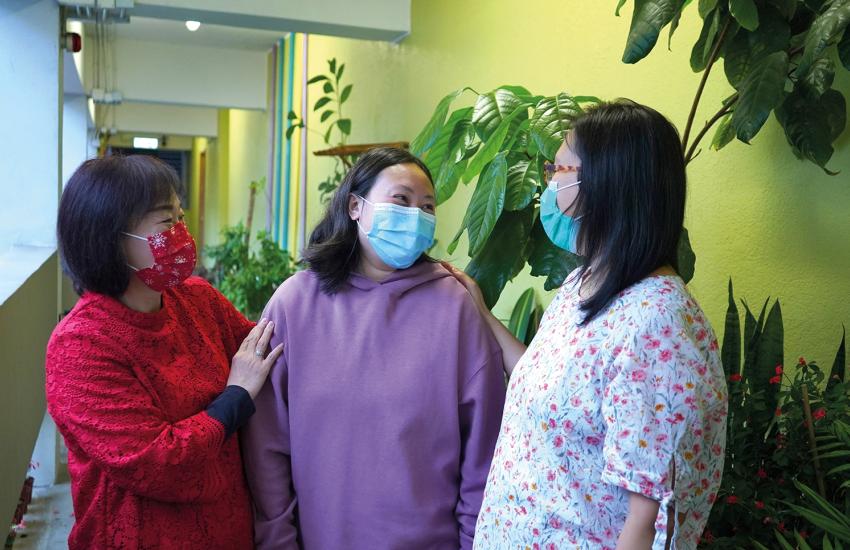 Three women, wearing facemasks, chat together