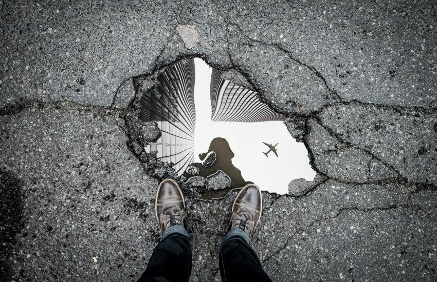 A man looks down at his reflection in a puddle